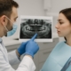 A dentist is showing a patient an x-ray of their jaw, pointing to the area where a bone graft for teeth implant may be needed. No text on image.