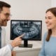 Image of a dentist explaining an x-ray of a patient's mouth, pointing to where dental implants would be placed. The patient is smiling and engaged.
